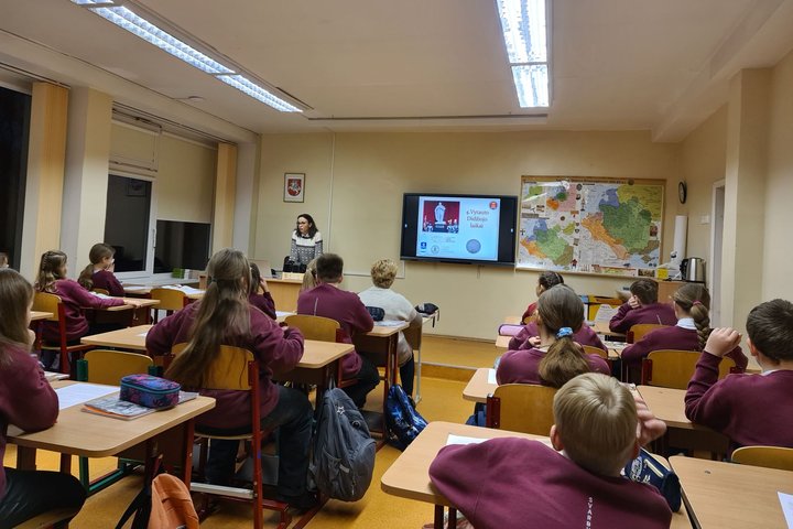 Klasėje, pilnoje mokinių, edukatorė veda istorijos pamoką.