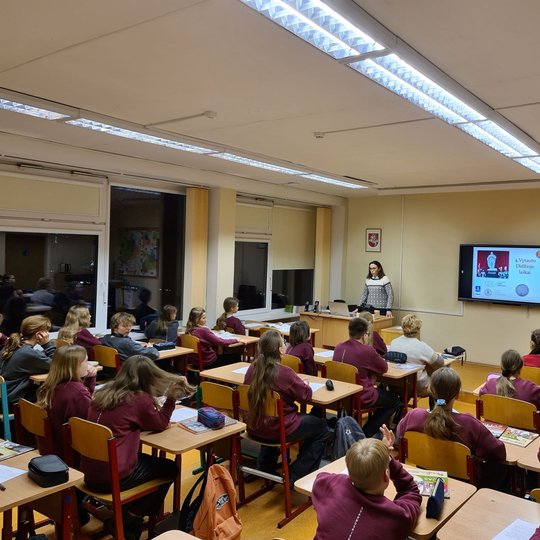 Klasėje, pilnoje mokinių, edukatorė veda istorijos pamoką.