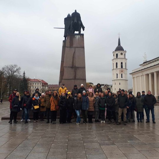 Visa ekskursijos grupė stovi Katedros aikštėje, prie pat kunigaikščio Gedimino paminklo.