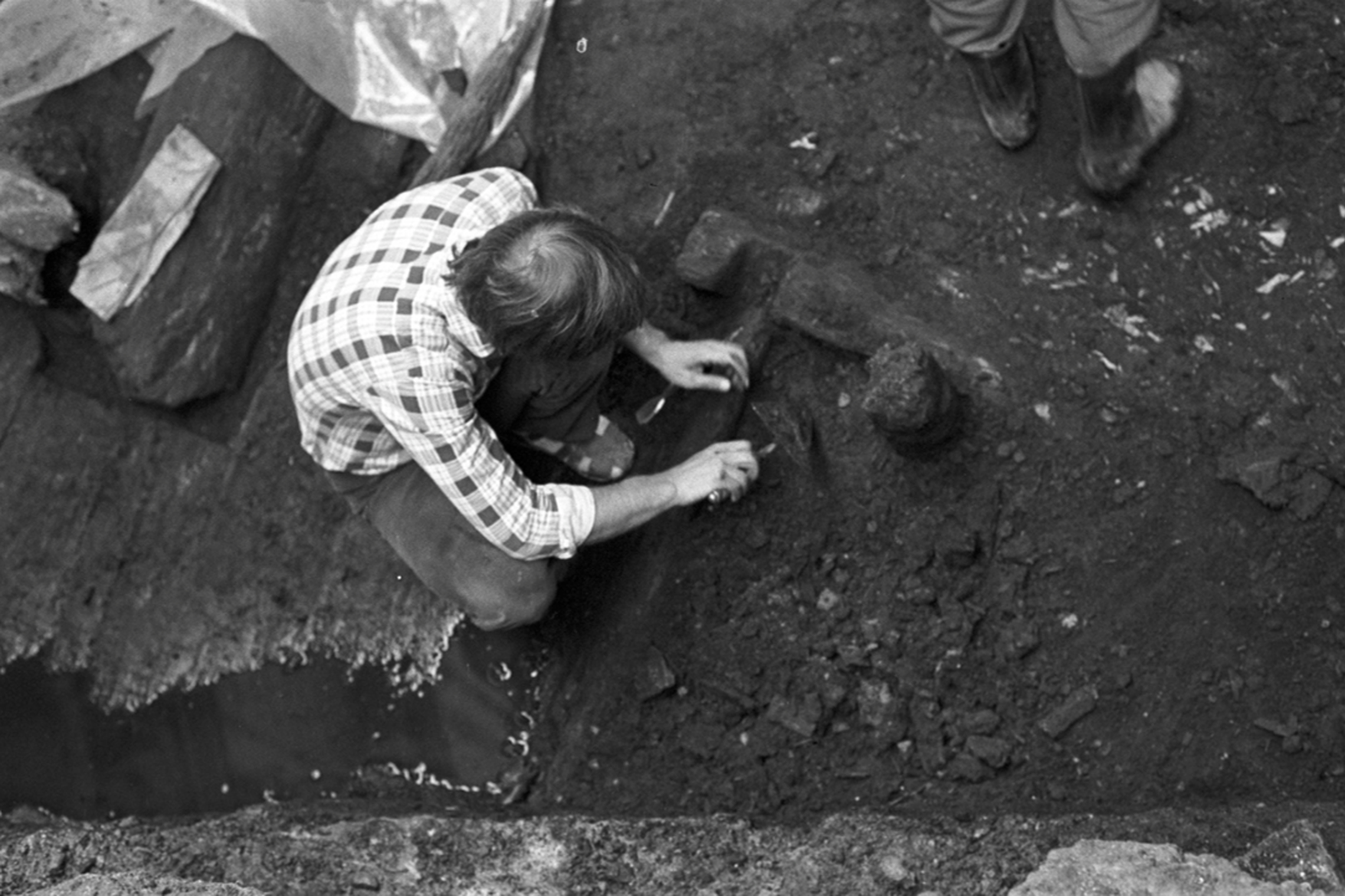 Nespalvota nuotraukoje, kurioje iš viršaus nufotografuotas jaunas archeologas Albinas Kuncevičius, atliekantis archeologinius kasinėjimus.