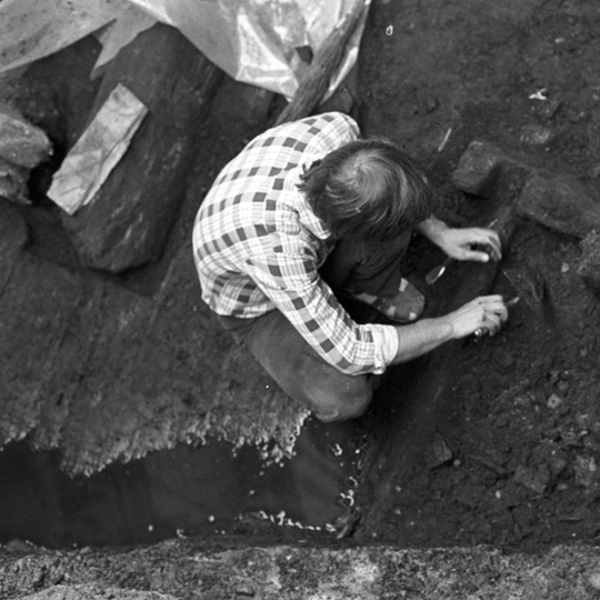 Nespalvota nuotraukoje, kurioje iš viršaus nufotografuotas jaunas archeologas Albinas Kuncevičius, atliekantis archeologinius kasinėjimus.