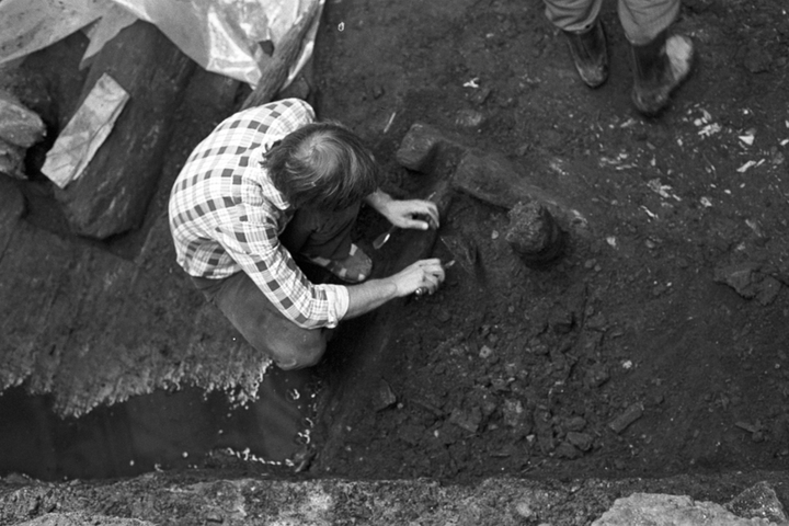Nespalvota nuotraukoje, kurioje iš viršaus nufotografuotas jaunas archeologas Albinas Kuncevičius, atliekantis archeologinius kasinėjimus.