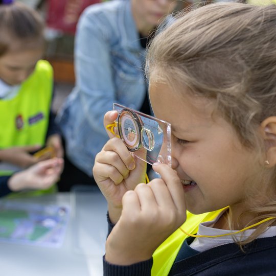 Mergaitė bando perprasti kompasą, žiūrėdama pro jį, kaip pro lupą.