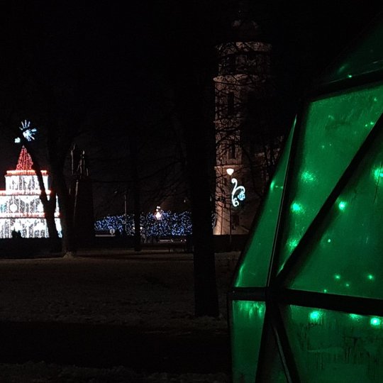 Tamsi nuotrauka, kurioje matosi žaliai šviečiantis Vilniaus pilių kupolo kamputis, tolumoje Vilniaus miesto kalėdinė eglutė bei katedros varpinės bokštas.