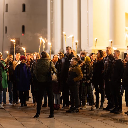 Ekskursijos būrys keliauja su fakelais priešais Arkikatedrą.