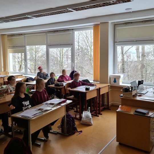 Edukatorė klasėje, pilnoje vaikų, veda istorijos pamoką.