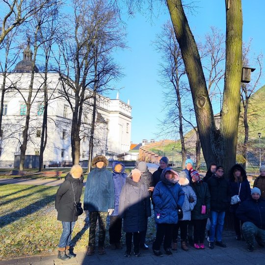"Mes esame" centro lankytojai stovi išsirikiavę Pilių parke. Jų fone - Valdovų rūmai ir Gedimino pilies kalnas.
