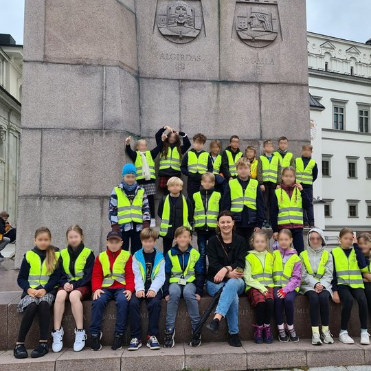 Mokinių grupė pozuoja susibūrusi prie Gedimino paminklo Katedros aikštėje.