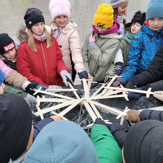 Mokiniai, virš geležinio Vilniaus pilių maketo, sudėję medinius kalavijus ratu.