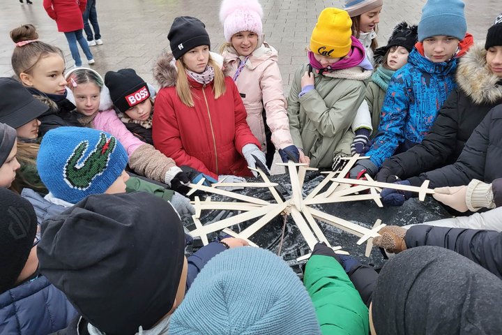 Mokiniai, virš geležinio Vilniaus pilių maketo, sudėję medinius kalavijus ratu.