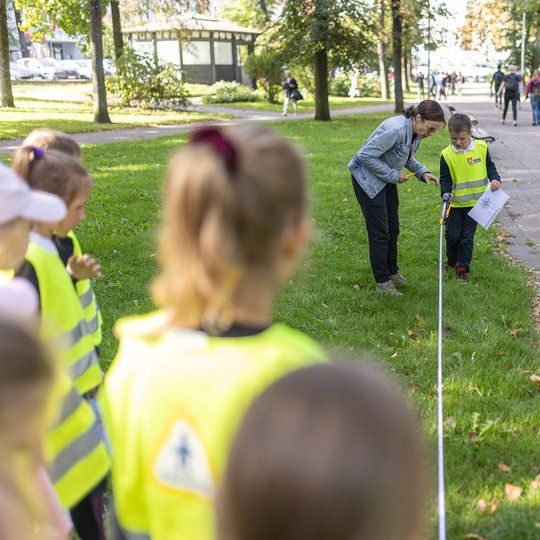 Vaikai, padedami edukatorės, rulete bando išmatuoti atstumą, kurį mato planuose.
