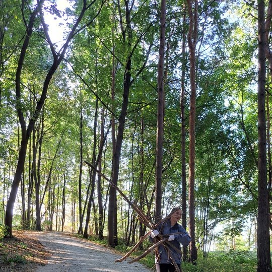 Nuotraukoje ant takelio stovi besišypsanti mergina, laikanti kelias šakas. Aplink ją medžiai. Ji yra Trijų kryžių kalne.