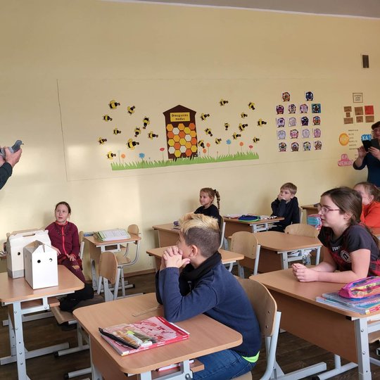 Edukatorius Stasys klasėje, priešais mokinius rodo karvelį.