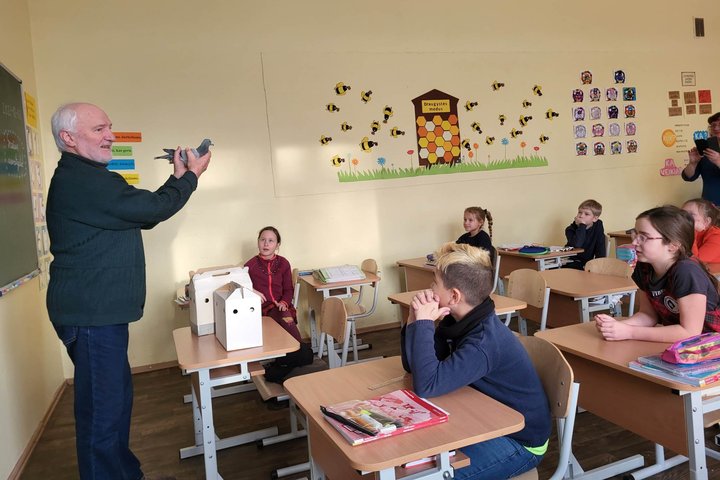 Edukatorius Stasys klasėje, priešais mokinius rodo karvelį.