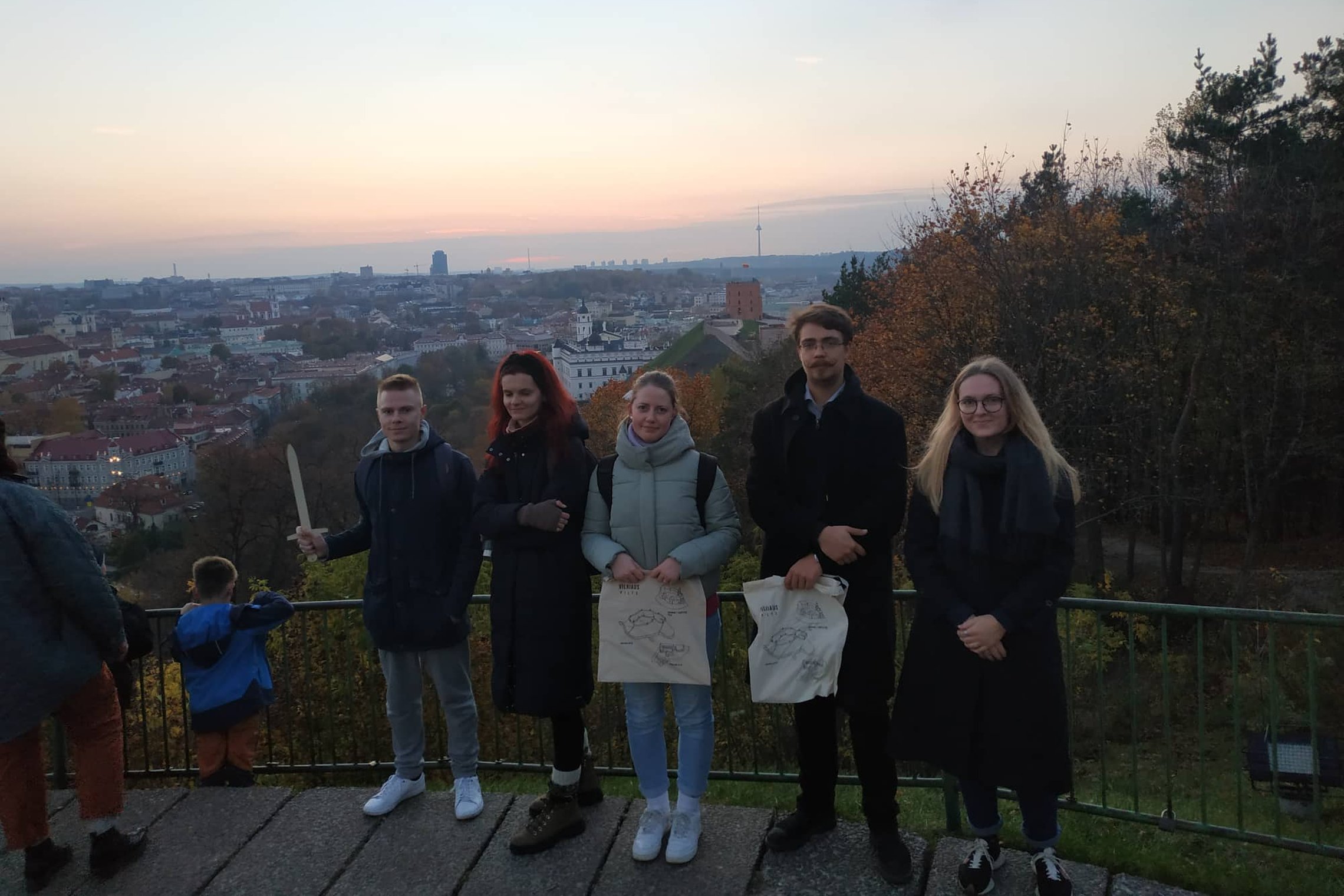 Draugai ir kolegos pozuoja nuotraukai priešais Trijų Kryžių paminklą. Už nugarų Gedimino kalnas su pilimi.