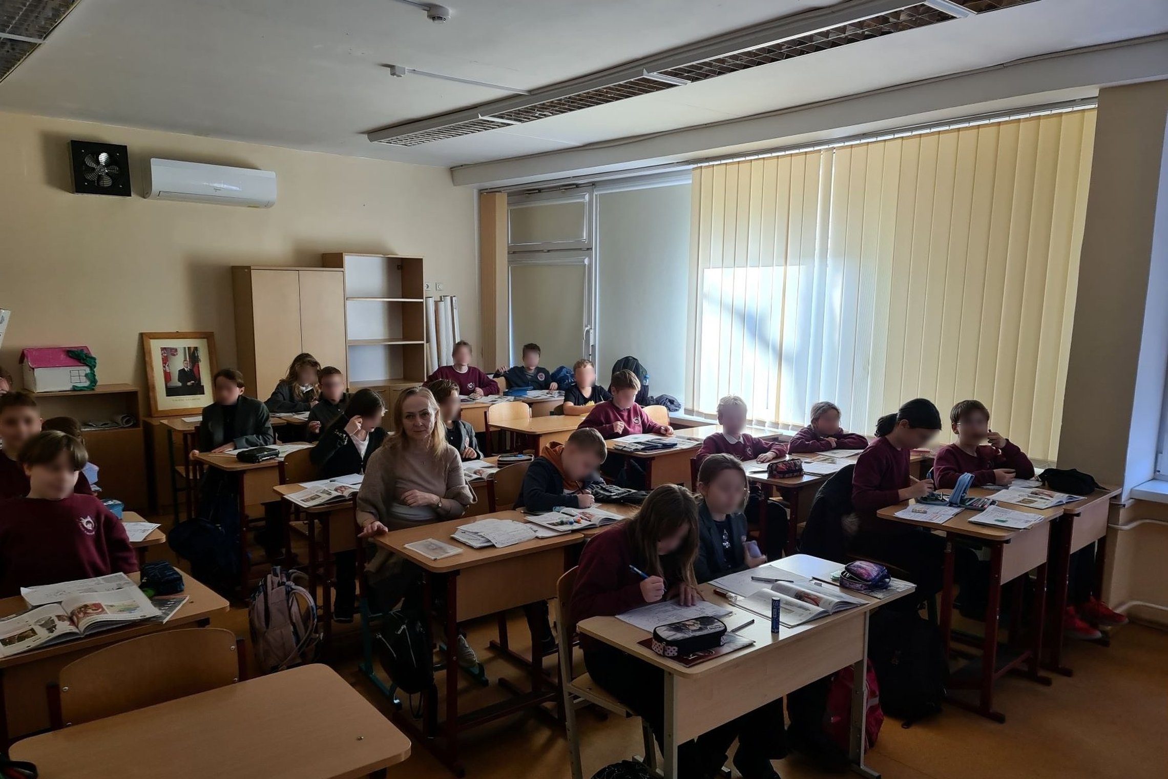 Penktokai sėdi klasės suoluose ir žiūri į kamerą.