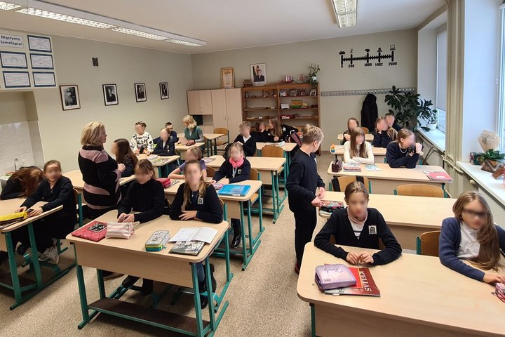 Vaikai ruošiasi istorijos pamokai klasėje. Tarp jų vaikšto ir mokytoja.
