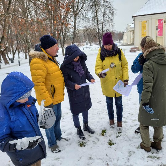 Edukacijos dalyviai šalia Lietuviškos baladės paminklo žiūri į žemėlapius.