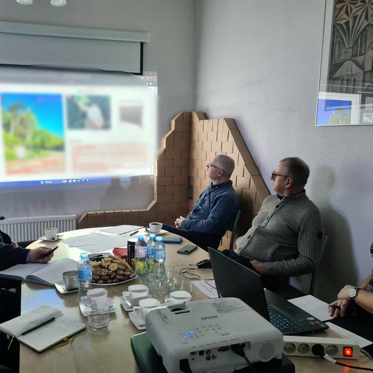 Stebima prezentacija, kol tarybos nariai, susėdę prie stalo, diskutuoja.