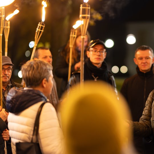 Gidė tarp ekskursijos dalyvių, kurie laiko fakelus.