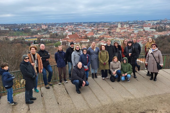 Ekskursijos dalyviai pozuoja nuotraukai priešais Trys Kryžius. Tolumoje matosi Vilniaus panorama.