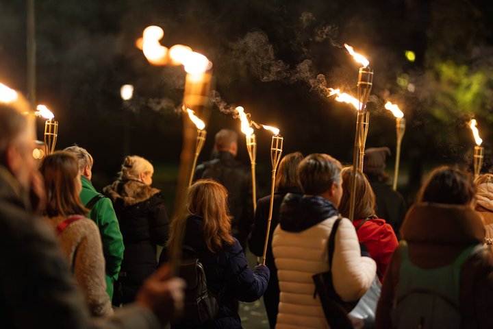 Ekskursijos dalyviai keliauja tamsoje su degančiais fakelais.