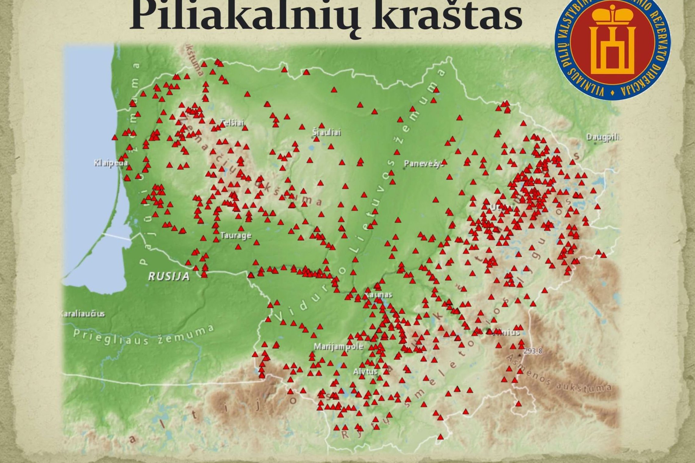 Nuotraukoje vaizduojamas "Piliakalnių krašto" Lietuvos žemėlapis. Žemėlapyje yra pažymėti didesni Lietuvos miestai ir daug raudonų mažų kvadratėlių, kurie žymi piliakalnių vietas. Dešinėje žemėlapio pusėje yra apvalus ženklas su užrašu "Vilniaus pilių val