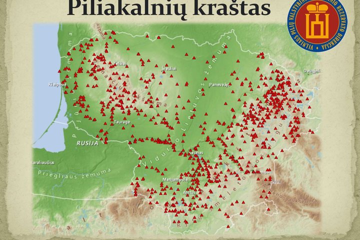 Nuotraukoje vaizduojamas "Piliakalnių krašto" Lietuvos žemėlapis. Žemėlapyje yra pažymėti didesni Lietuvos miestai ir daug raudonų mažų kvadratėlių, kurie žymi piliakalnių vietas. Dešinėje žemėlapio pusėje yra apvalus ženklas su užrašu "Vilniaus pilių val