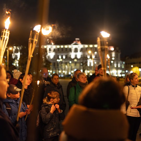 Gidė tarp ekskursijos dalyvių, kurie laiko fakelus.