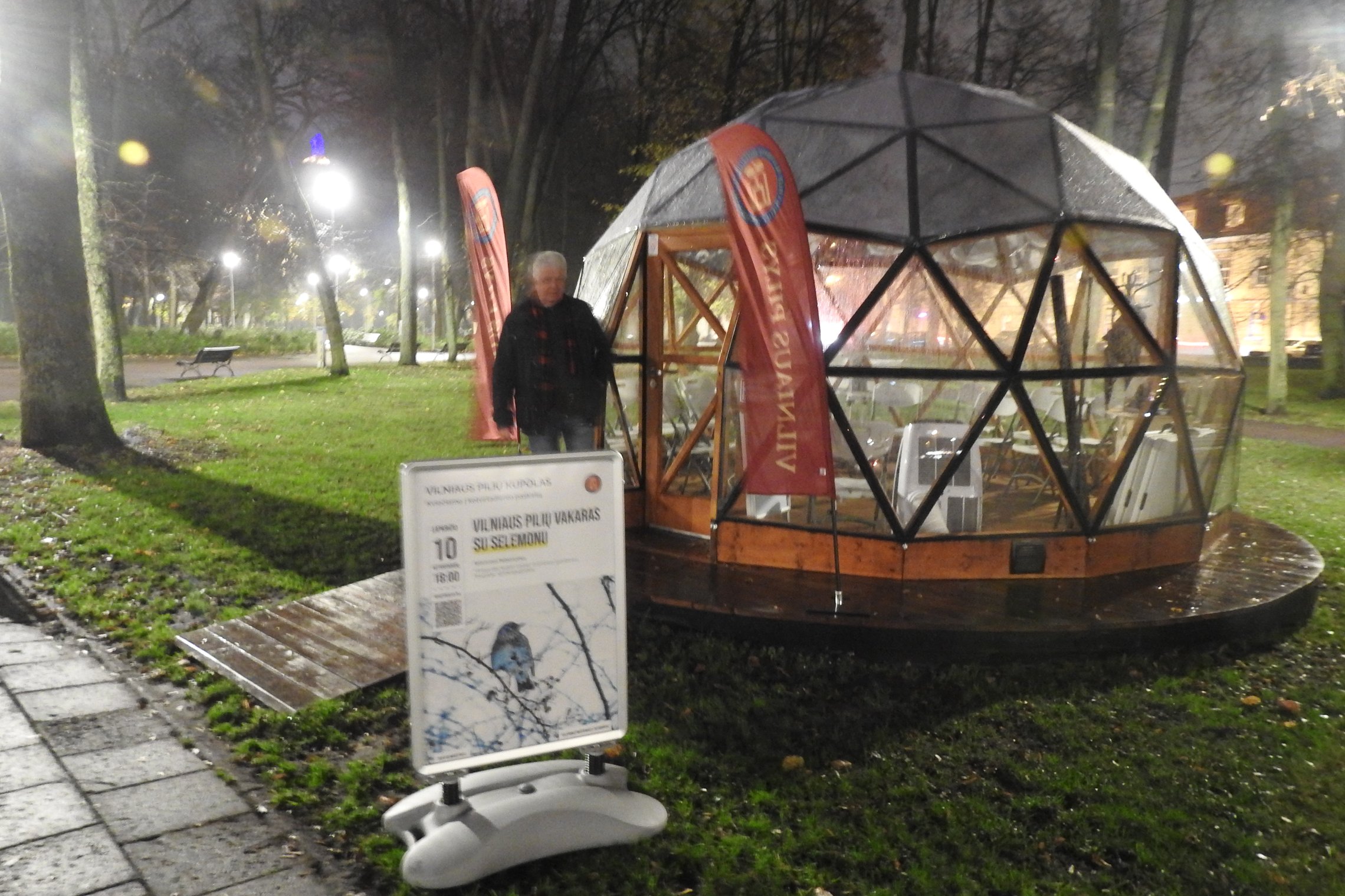 Vilniaus pilių kupolas iš lauko. Priešais kupolą paskaitos afiša. Prie įėjimo stovi aplinkosaugininkas Selemonas Paltanavičius.