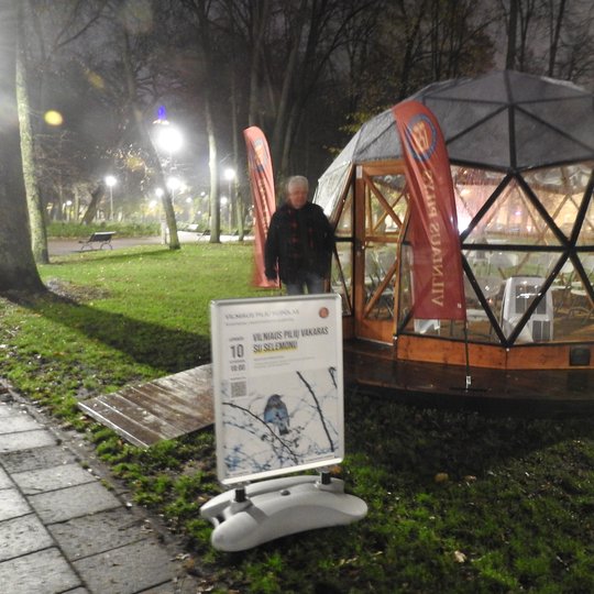 Vilniaus pilių kupolas iš lauko. Priešais kupolą paskaitos afiša. Prie įėjimo stovi aplinkosaugininkas Selemonas Paltanavičius.