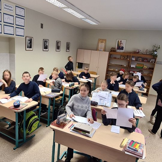 Vaikai klasėje aktyviai varto sąsiuvinius ir baltus lapus.