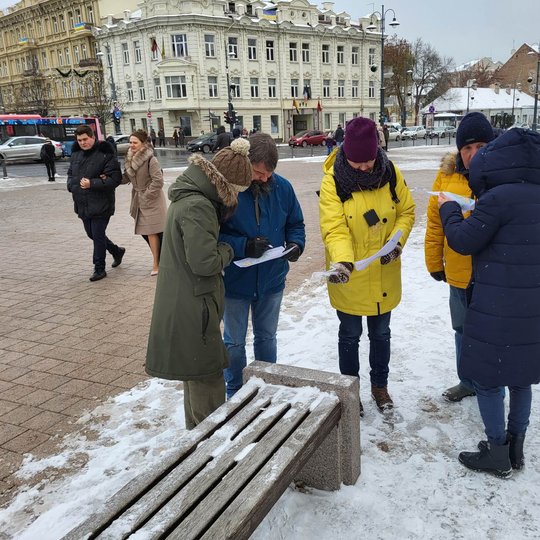 Edukacijos dalyviai šalia katedros varpinės bokšto suoliukų orientuojasi žemėlapyje. 