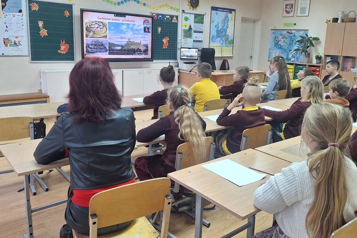 Trečiokai klasės suoluose stebi, ką jiems per projektoriaus vaizdą pasakoja ir rodo Vilniaus pilių edukatorė.