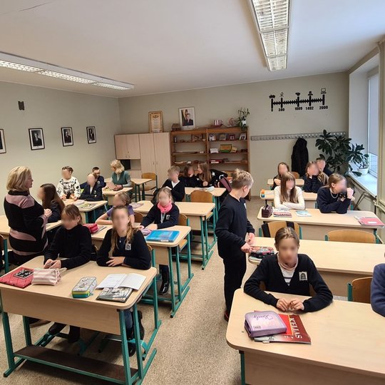 Vaikai ruošiasi istorijos pamokai klasėje. Tarp jų vaikšto ir mokytoja.
