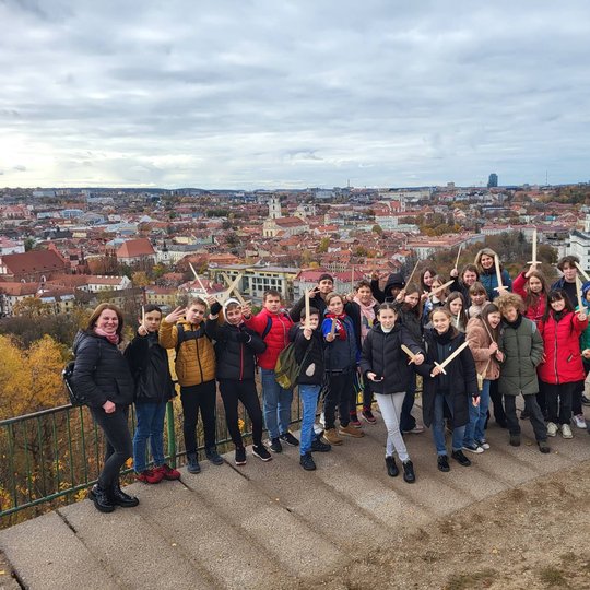 Vilniaus Naujininkų progimnazijos šeštokai pozuoja nuotraukai su mediniais kalavijais priešais Trijų Kryžių paminklą. Už nugarų Vilniaus panorama.