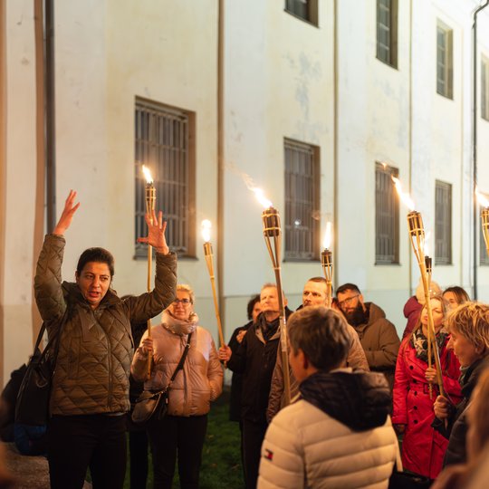 Gidė tarp ekskursijos dalyvių, kurie laiko fakelus.