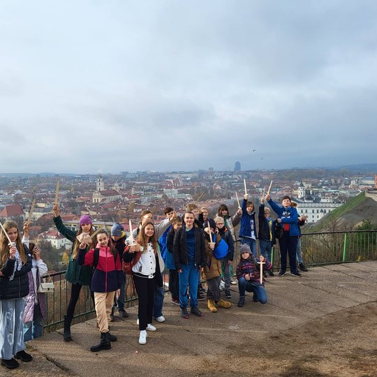Mokiniai pozuoja nuotraukai ant Trijų Kryžių kalno. Tolumoje matosi Vilniaus panorama.