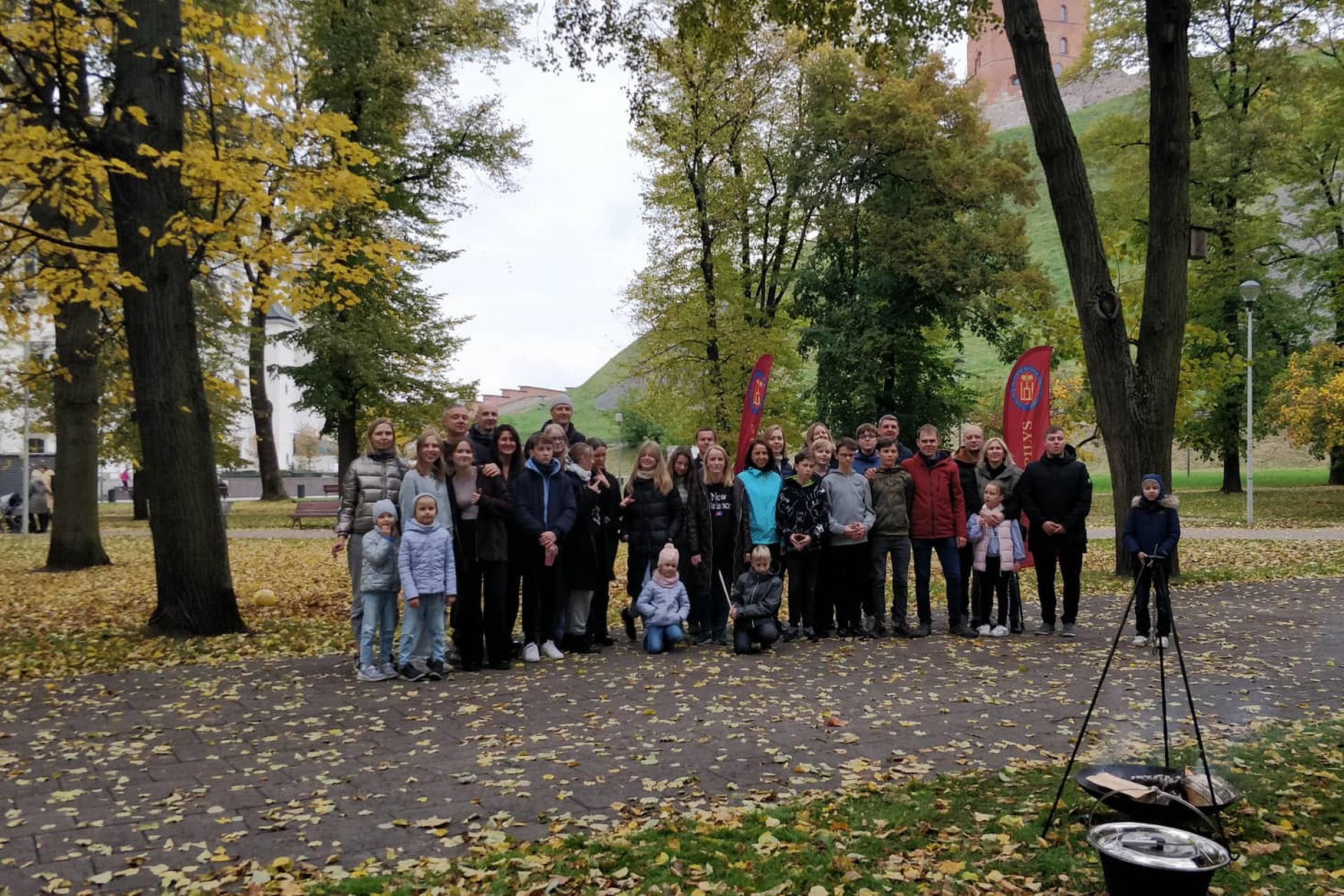 Vilniaus jėzuitų gimnazijos septintokai ir jų tėveliai Pilių parke pozuoja bendrai nuotraukai. Dešinėje viršuje Gedimino pilies bokštas.