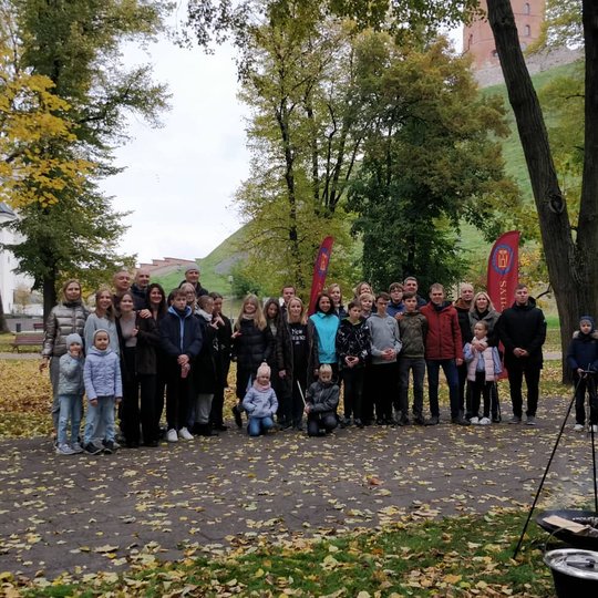 Vilniaus jėzuitų gimnazijos septintokai ir jų tėveliai Pilių parke pozuoja bendrai nuotraukai. Dešinėje viršuje Gedimino pilies bokštas.