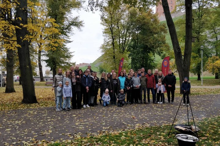 Vilniaus jėzuitų gimnazijos septintokai ir jų tėveliai Pilių parke pozuoja bendrai nuotraukai. Dešinėje viršuje Gedimino pilies bokštas.