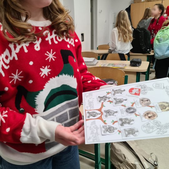 Mergaitė, apsirengusi kalėdiniu megztiniu, laiko savo sukurtą genealoginį valdovų medį.