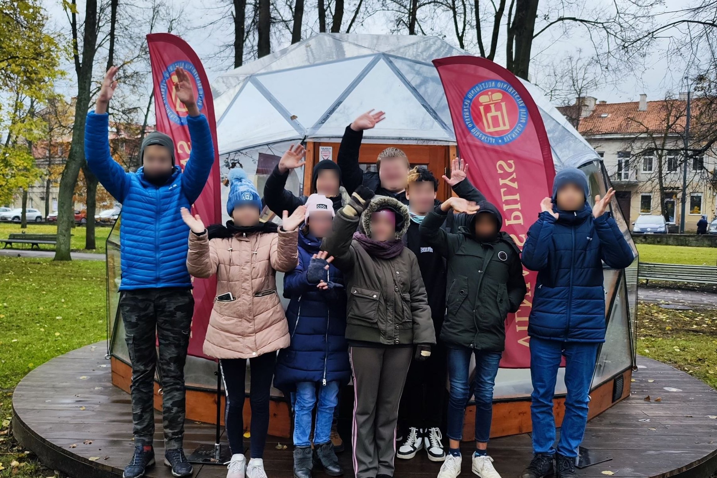 Vilniaus Verkių mokyklos mokiniai mojuoja į kamerą, sustoję prie Vilniaus pilių kupolo.