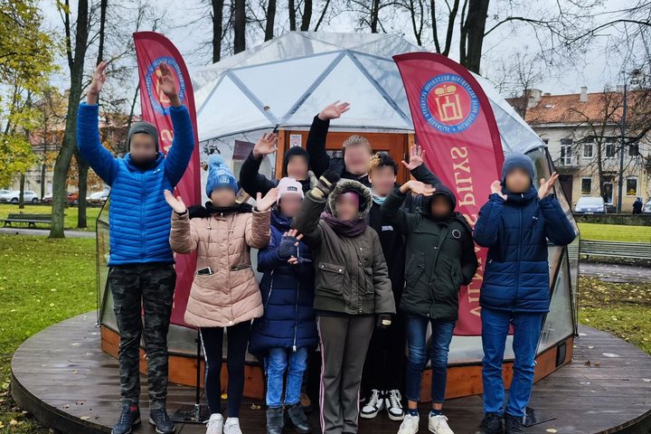 Vilniaus Verkių mokyklos mokiniai mojuoja į kamerą, sustoję prie Vilniaus pilių kupolo.