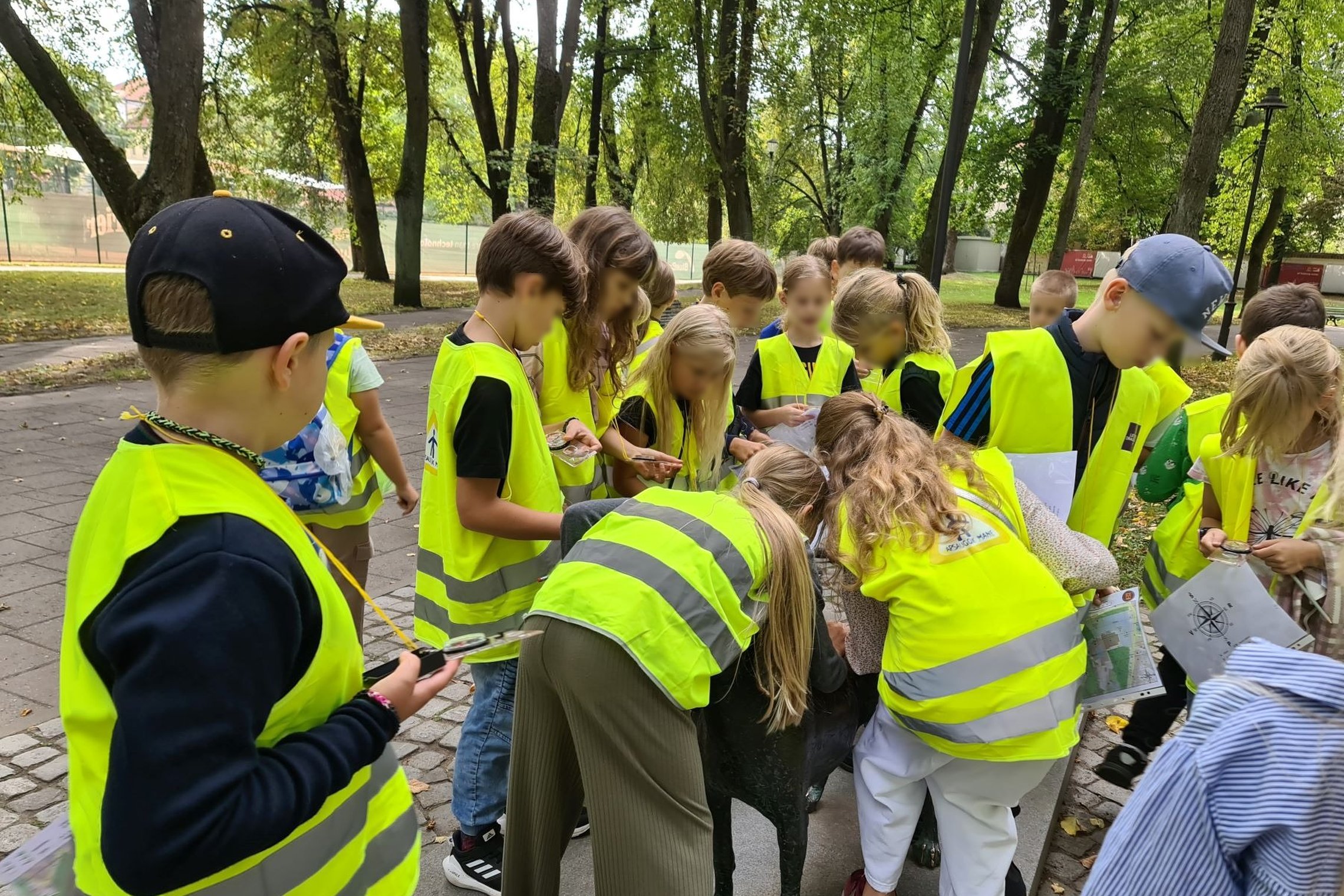 Vilniaus mokyklos mokiniai, mažieji smalsuoliai trečiokai, apsirengę ryškiomis, žaliai-geltonomis liemenėmis, apžiūrinėja gyvūno pavidalo paminklą. Įdėmiai žvelgia į kompasą ir tyrinėja žemėlapį.