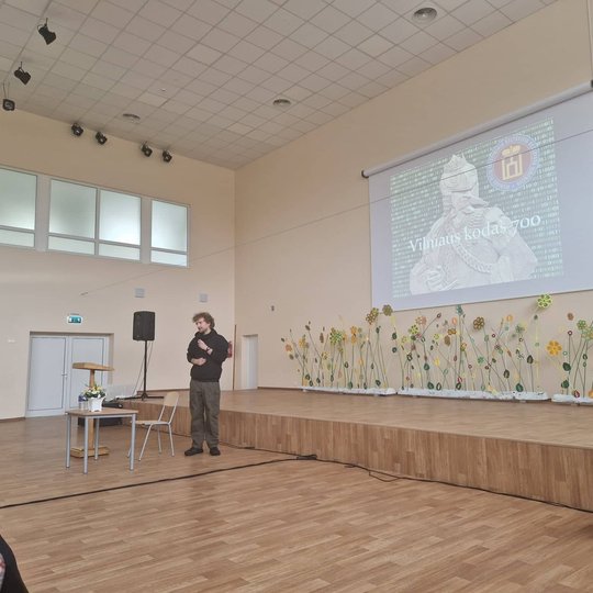 Edukatorius Vytas Navickas Akademijos gimnazijos aktų salėje skaito pranešimą. Už nugaros skaidrė su kunigaikščio Gedimino biustu. 