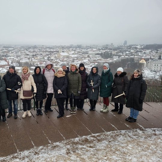 „Vilniaus senojo teatro" kolektyvas pozuoja nuotraukai priešais Trijų Kryžių paminklą. Jiems už nugarų Vilniaus miesto panorama.