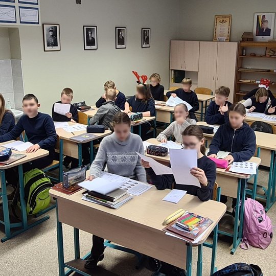 Vaikai klasėje aktyviai varto sąsiuvinius ir baltus lapus.