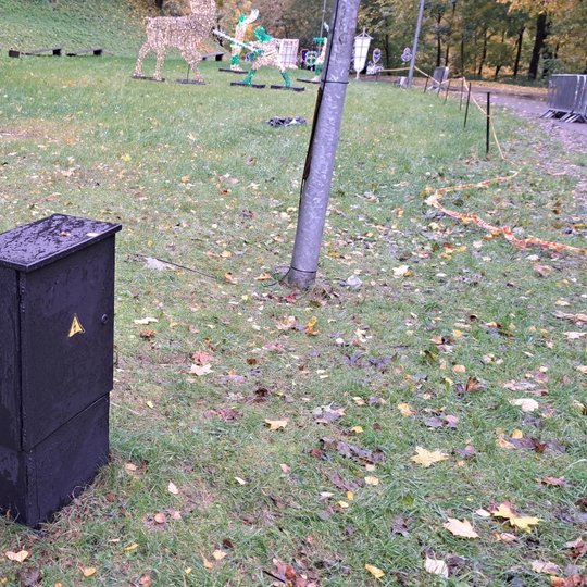 Matoma juoda, švari elektros skydinė. Už jos yra lauko suolai ir šviesų instaliacijos Kalnų parke.