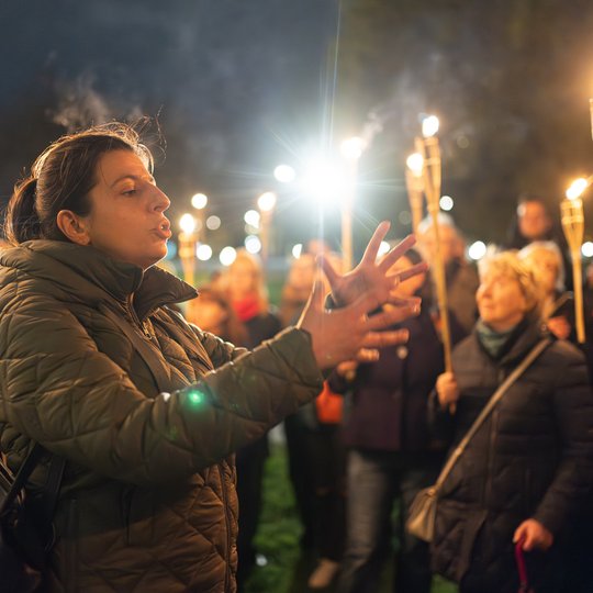 Gidė tarp ekskursijos dalyvių, kurie laiko fakelus.